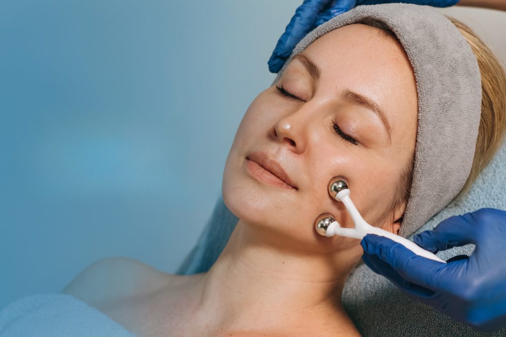 Beauty therapist treating a client's face with metal massage wands – signature facial in Vienna